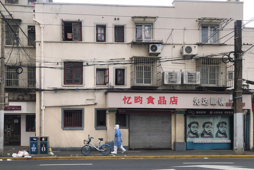 A worker in protective gear walks along shuttered shops in the Jingan district under lockdown in western Shanghai