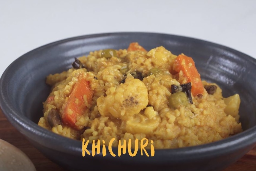 A bowl of Khichuri. The bowl is black and the ingredients include carrots, cauliflower, rice and lentils.