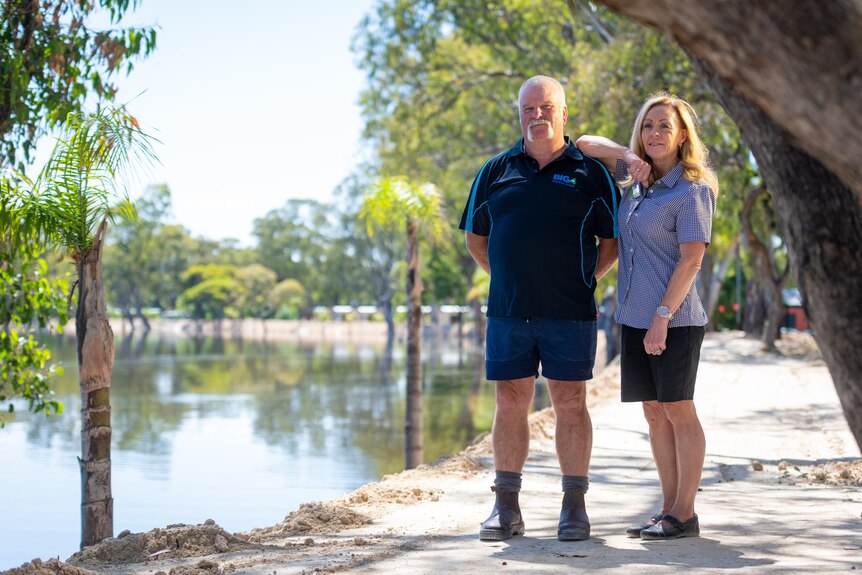 A man and a woman standing on the ground next to a river