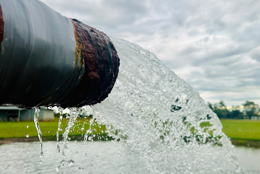 A rusted pipe pushes out hot water into a small pond