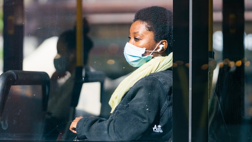 A young women wearing a face mask looks out of a window on board a Transperth bus within the CBD.