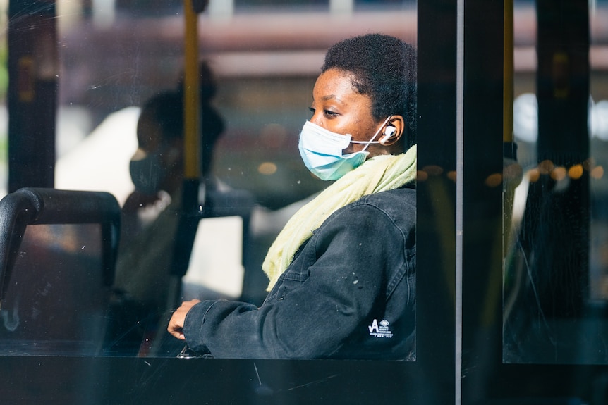 A young woman wearing a face mask looks out of a window aboard a Transperth bus in the CBD.