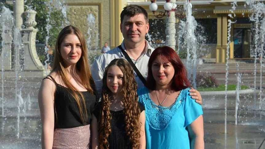 A Ukrainian family stand together on a summer's day near a fountain. Two daughters and a mother and father.