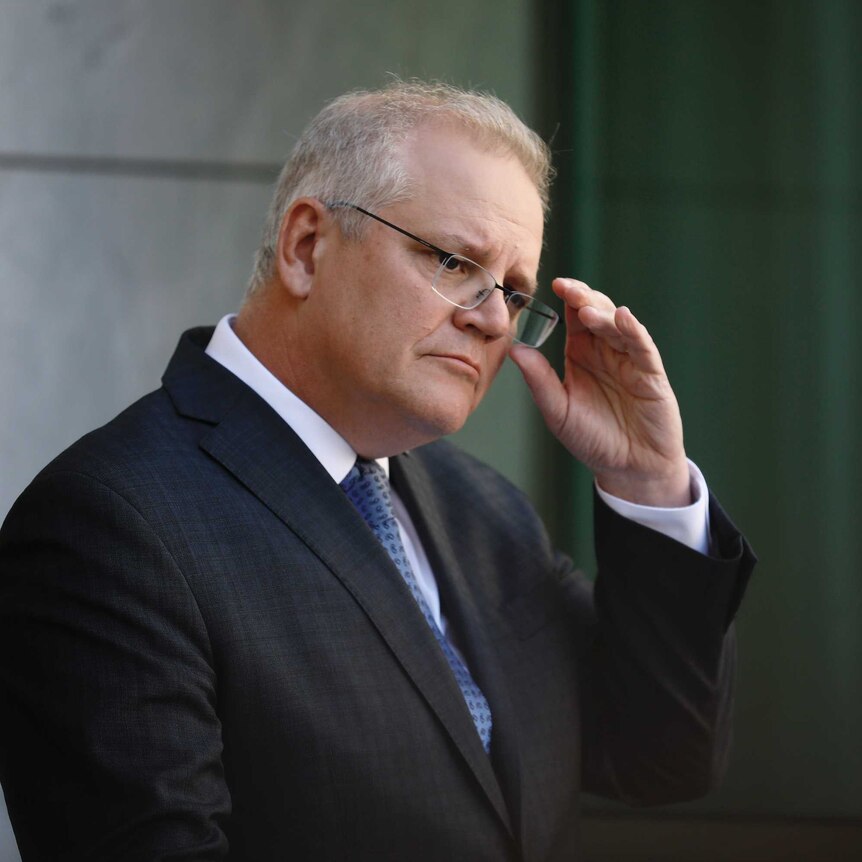 Morrison adjusts his glasses with his left hand.
