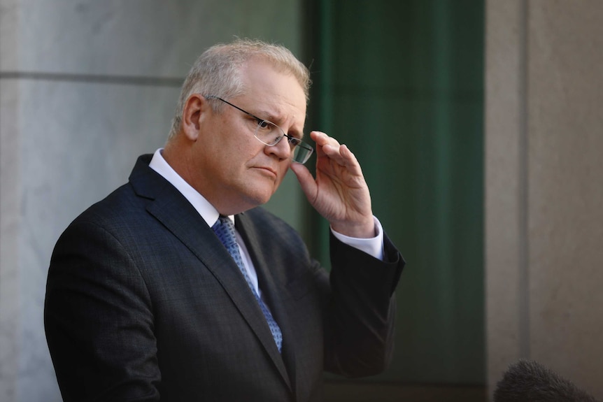 Morrison adjusts his glasses with his left hand.