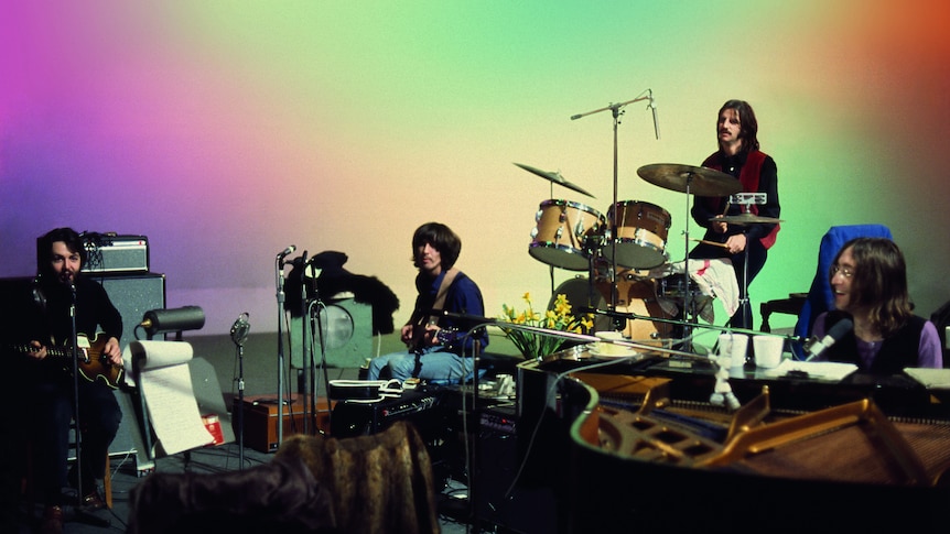 The Beatles band playing in front of a rainbow backdrop