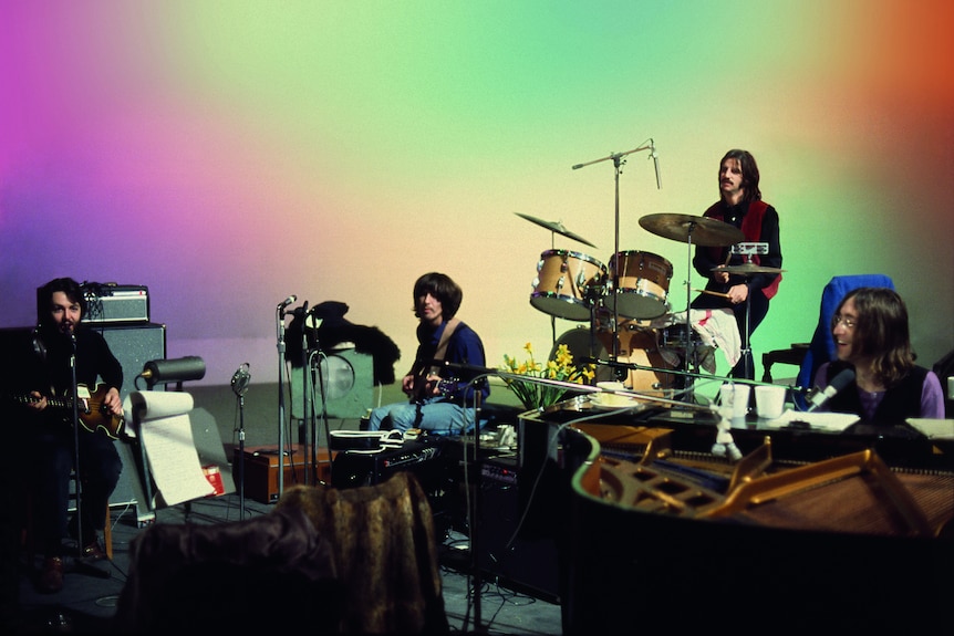 The Beatles band playing in front of a rainbow-coloured backdrop.