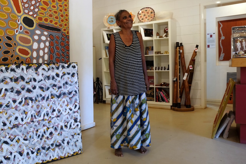 A woman stands in the middle of an Indigenous art gallery.