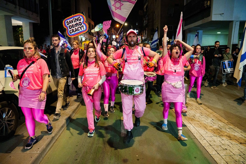 A group of protesters dressed in pink waves flags and banners as they march on a street.