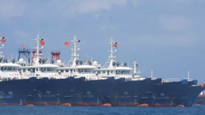 A close shot of a row of large fishing vessels with Chinese writing seen on the side.