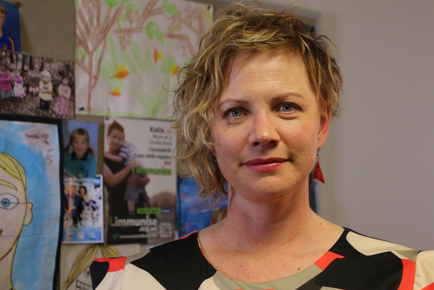 Katie Attwell standing in a room with bright drawings and brochures on the wall.