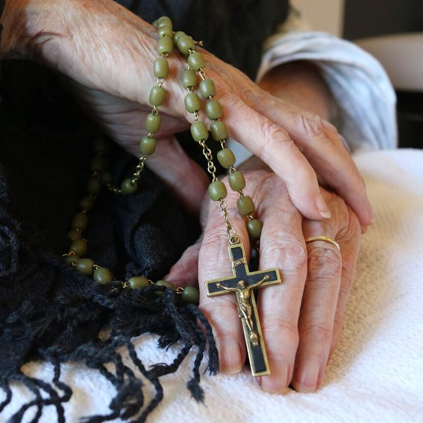 An elderly woman holds rosary beads.