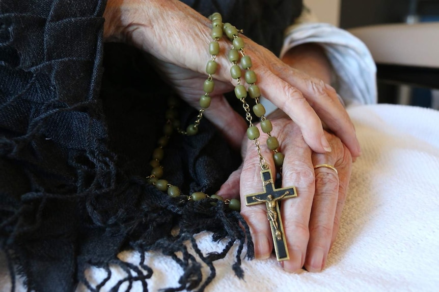 An elderly woman holds rosary beads.