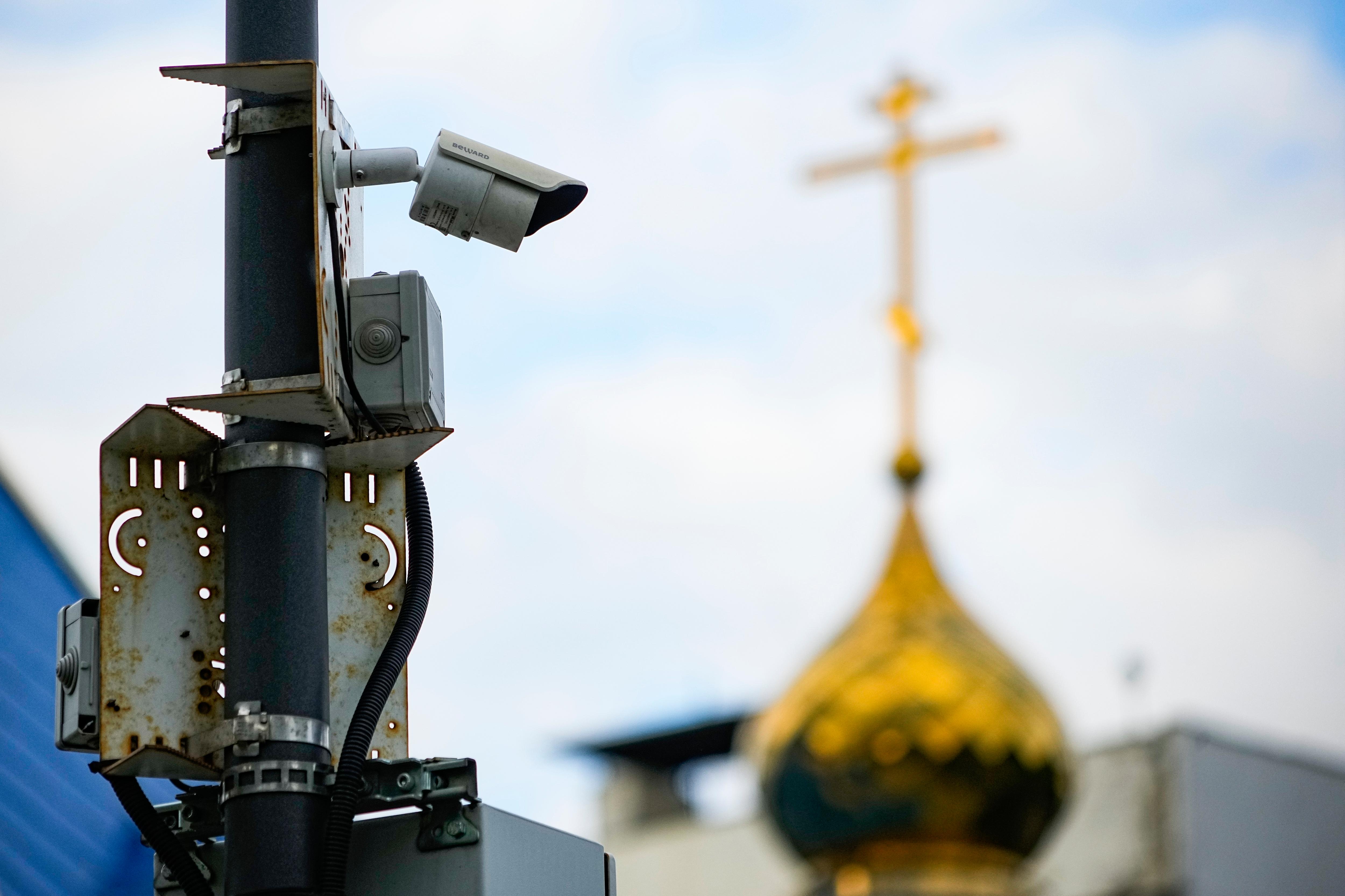 A surveillance camera sits on a utility pole, with the top of a Russian orthodox church in the background.