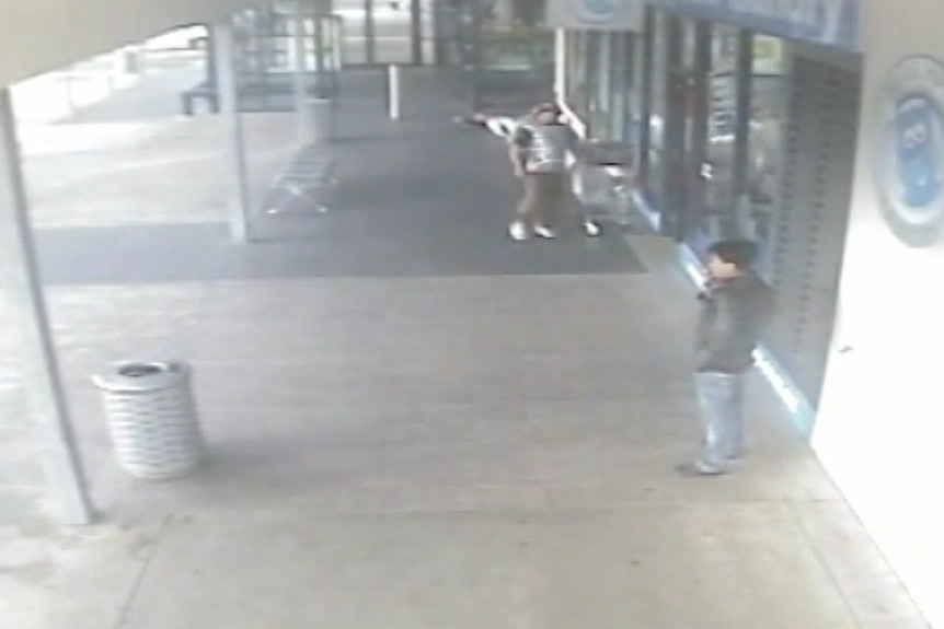 A grainy shot from CCTV shows a man walking away from a man lying on the ground.