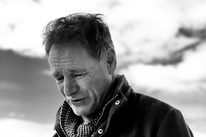 a black and white photo of a man wearing a jacket and scarf looking down away from the camera