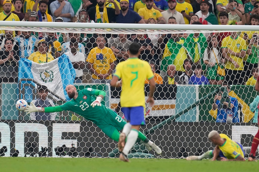 Serbian goalkeeper Vanja Milinkovic-Savic dives to try to stop Richarlison's goal for Brazil at the Qatar World Cup.