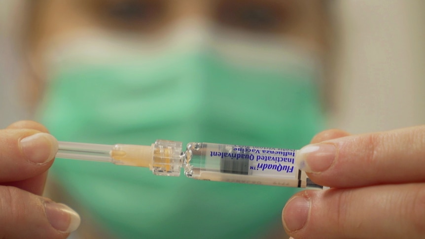 A nurse in a mask holds a vial of flu vaccine.