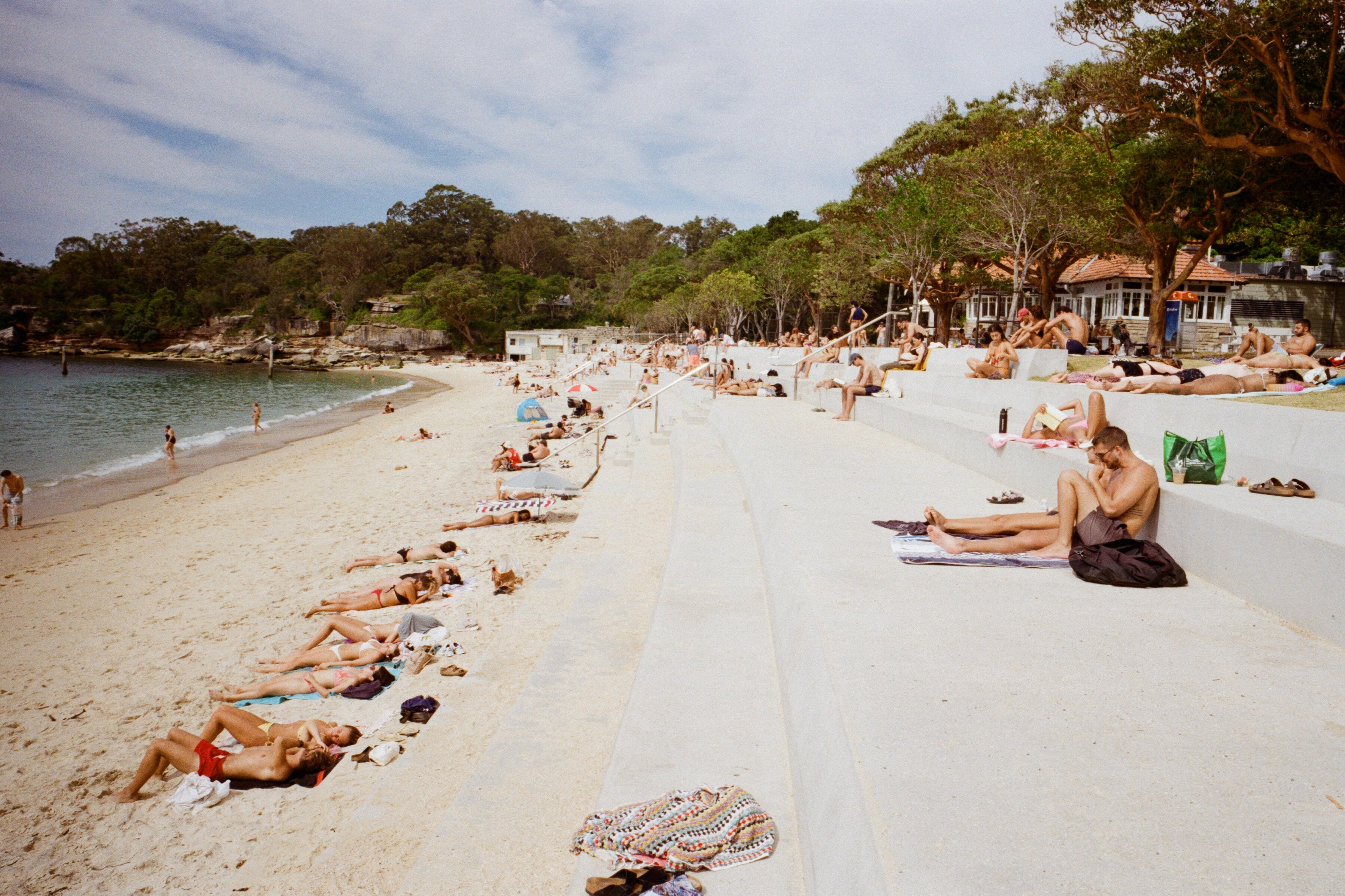 Beachgoers suntan and sit on the sand on a hot day, while others swim in the ocean.