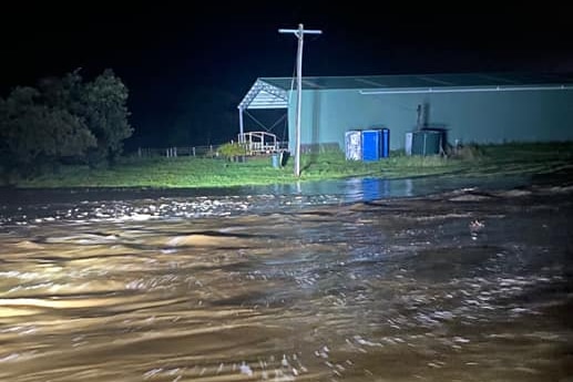 Floodwater rushing past a farm storage shed.