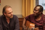 Actors Hugo Weaving and Andrew Luri in Hearts and Bones sitting in a hall, Andrew playing guitar