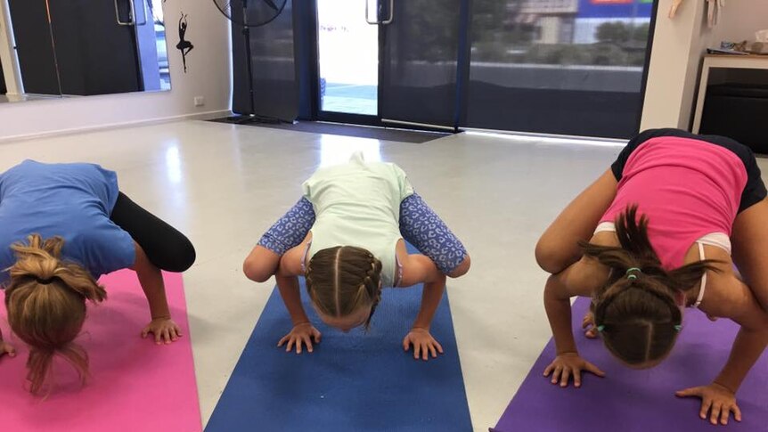 Three girls practising a yoga pose with their legs balanced on their arms.