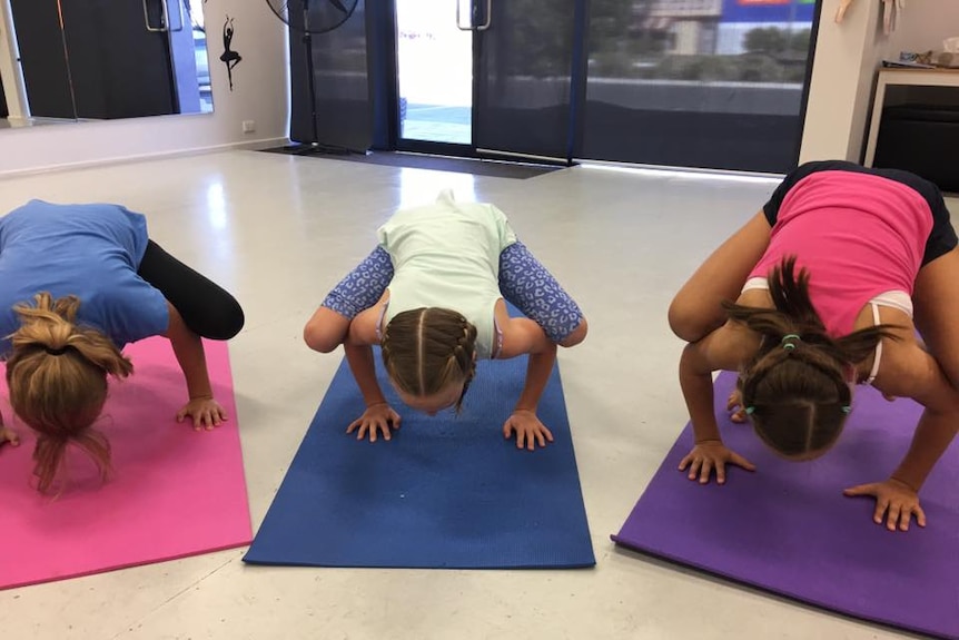 Three girls practising a yoga pose with their legs balanced on their arms.