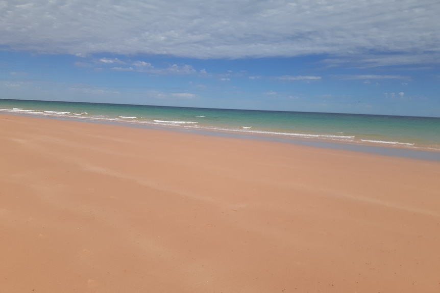 Golden sand and blue green water under a blue sky speckled with high cloud