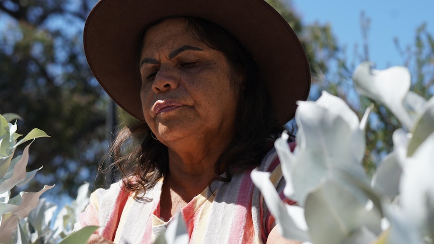An Indigenous woman with a broad rim hat smells flowers