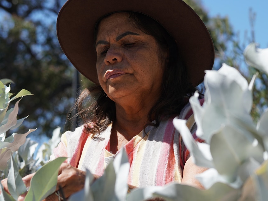 An Indigenous woman with a broad rim hat smells flowers