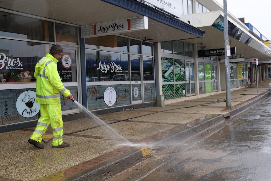 A council worker in a yellow hazmat suit hosing down pathways in Port Macquarie CBD. 