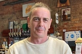 A picture of a man in a white jumper standing in front of a bar.