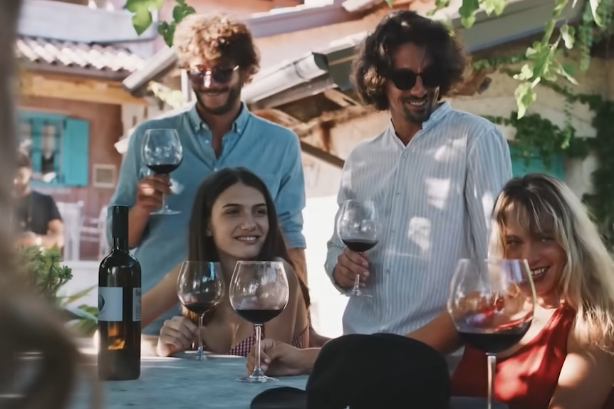 People drinking wine around table and smiling.