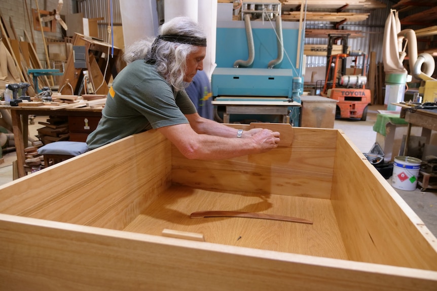 A man adds pieces to a wooden storage chest.