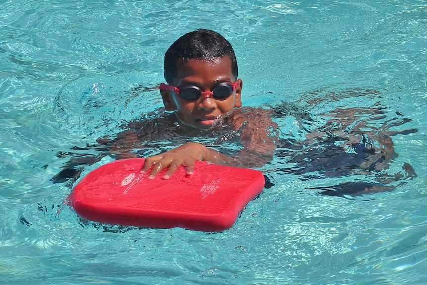 A young swimmer kicks as they hold onto a floating device