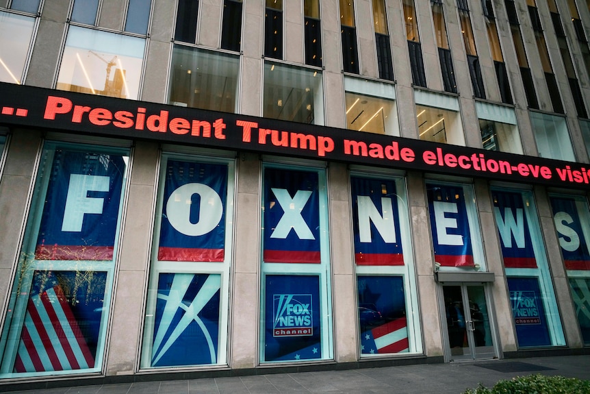 Large letters spelling FOX NEWS fill windows of an office building, while an electronic message reads "President Trump..."