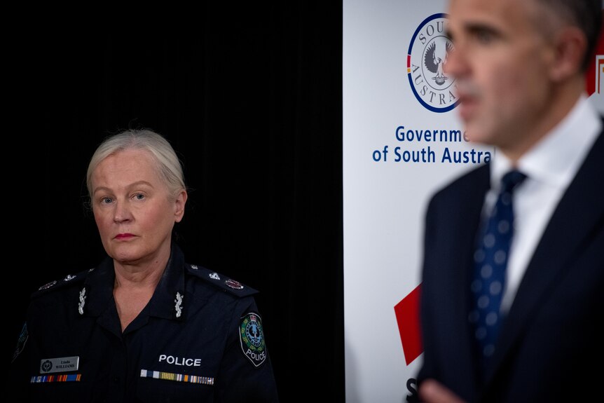 A woman in a police uniform looking at a man speaking in front of a banner