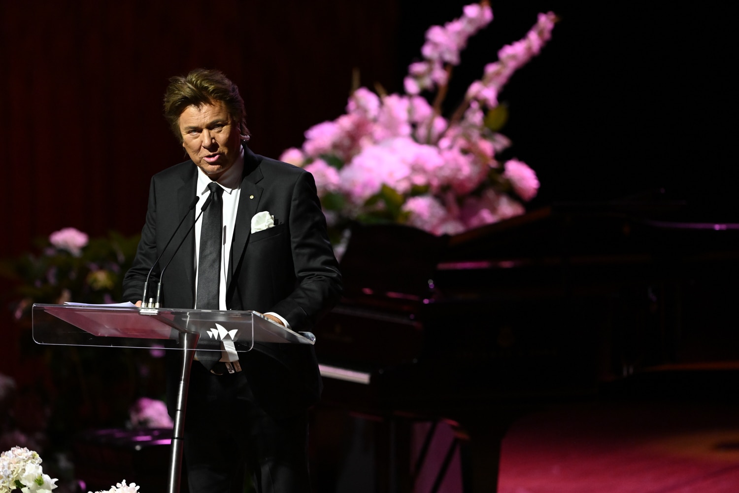 An older man in a suit speaks on stage.