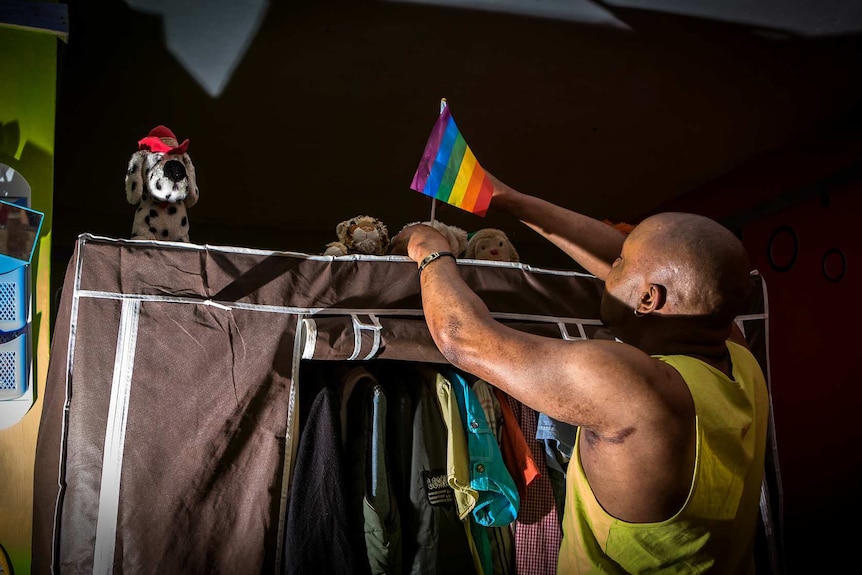 Mama G fixes a pride flag above the wardrobe in his apartment.
