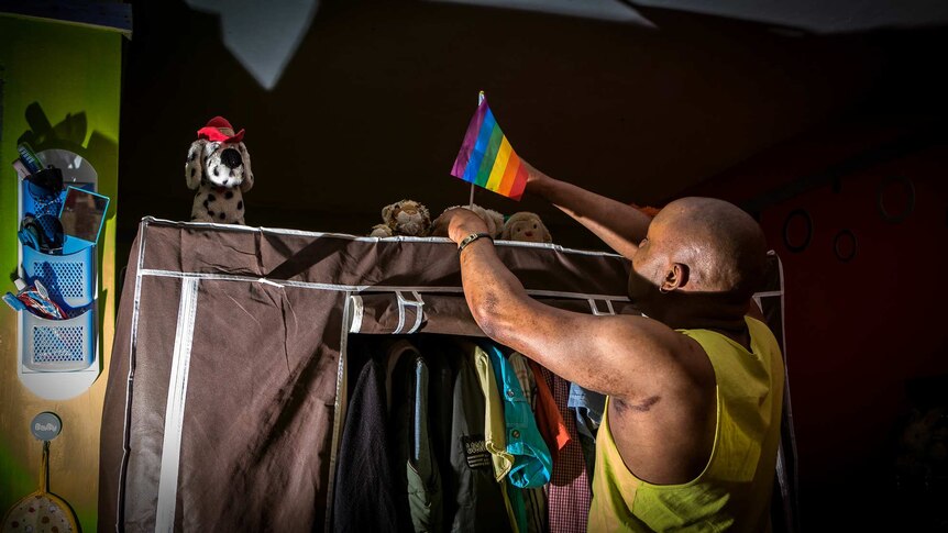 Mama G fixes a pride flag above the wardrobe in his apartment.