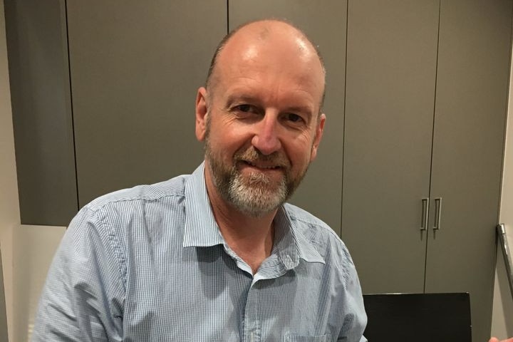 A middle-aged bald man with a beard wearing a blue shirt while sitting down