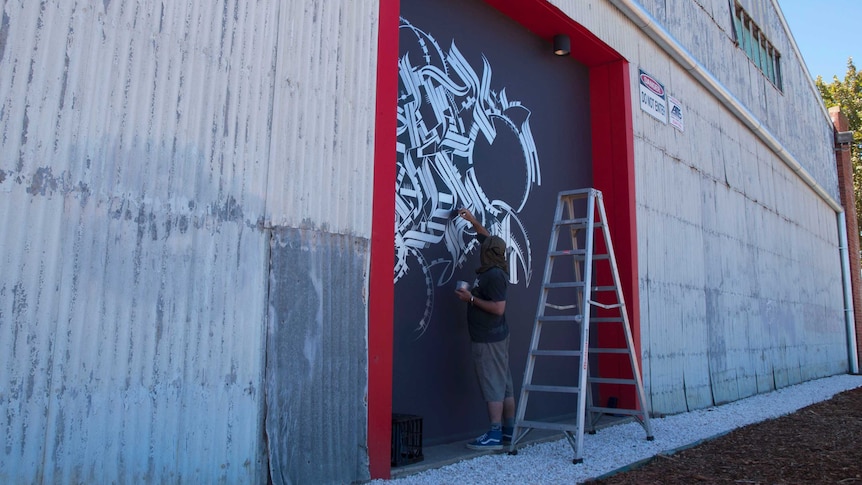 Port Adelaide artist Kab101 brush-paints the door of a warehouse on Mundy Street.