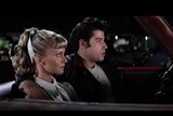 Screengrab from the movie Grease showing the leather-jacket wearing Danny with his arm around Sandy in a convertible car.
