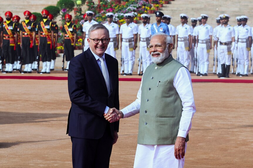 Anthony Albanese (left) shakes hands with Narendra Modi while both look at cameras.