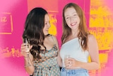 Two young women grin, holding champagne glasses.