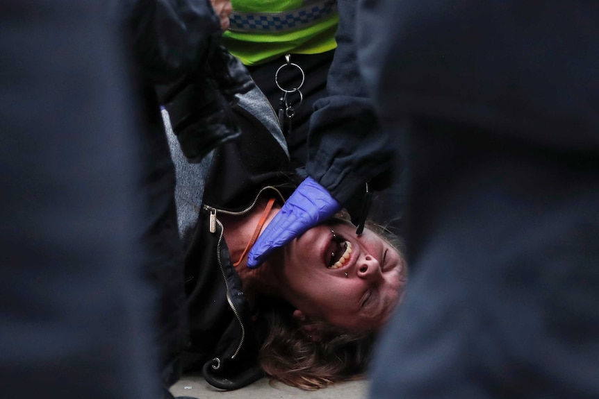 A person is is laying on the ground and a police officer's gloved hand is holding them down
