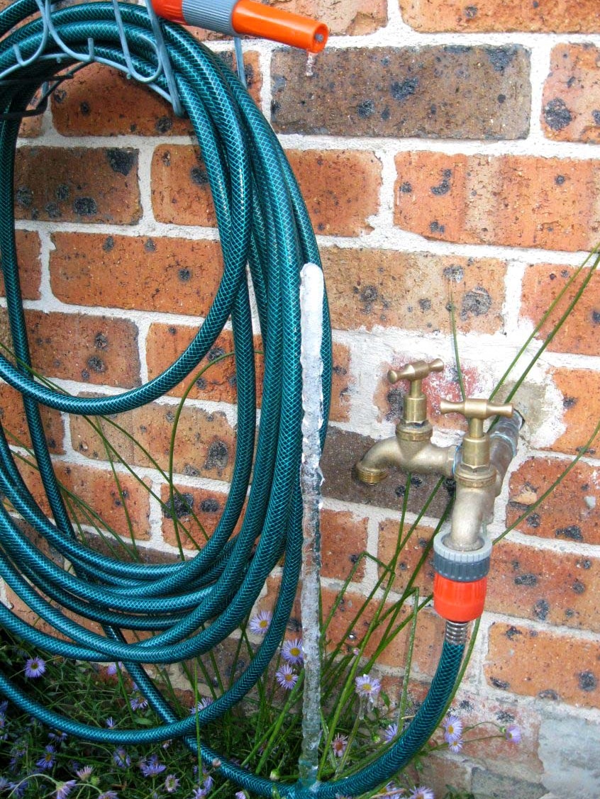 An ice spike forms on a garden hose at a house on a freezing morning.