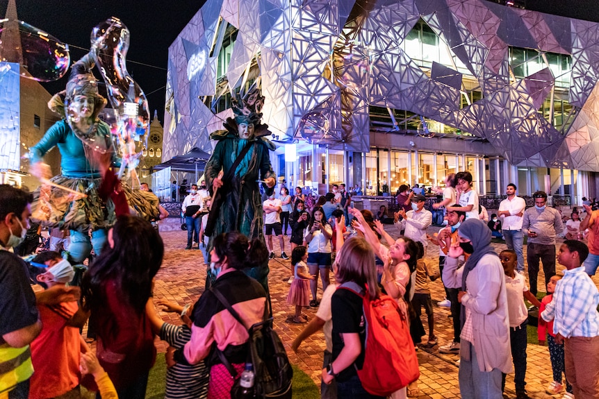 Performers on stilts weave bubbles and entertain the crowd at Melbourne's Federation Square