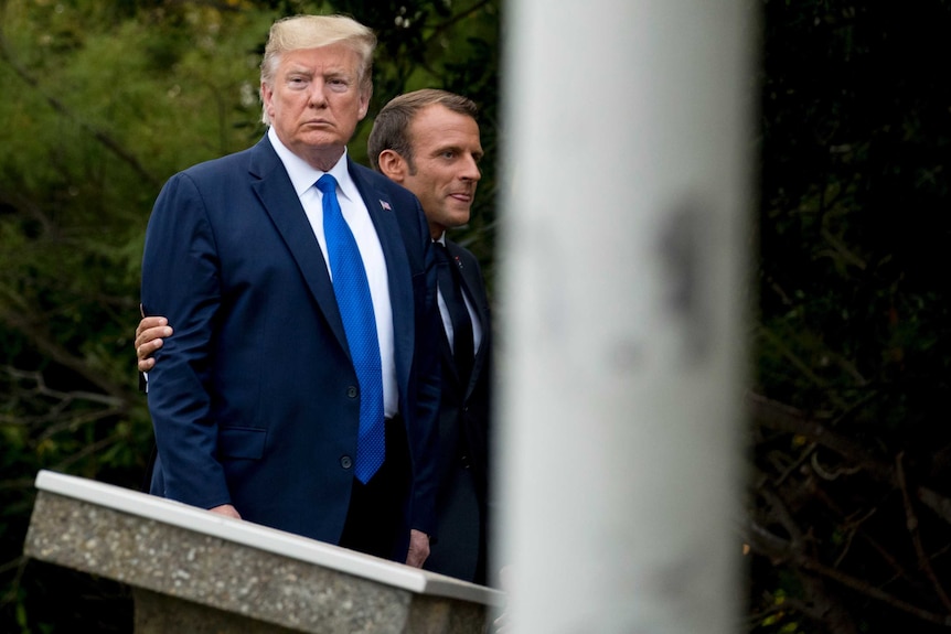 Donald Trump looks away as Emmanuel Macron puts his arm around him as they walk at the G7 summit