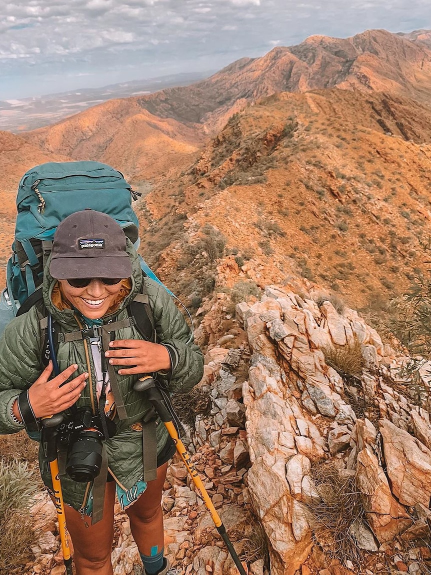 A woman with a hiking pack with a mountain range in the background.